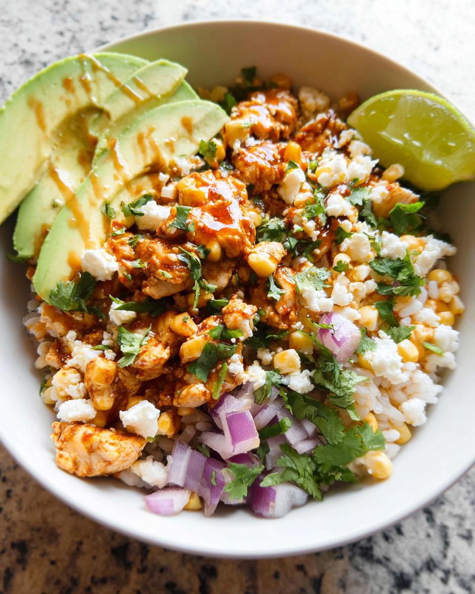 A close-up of an Easy Street Corn Chicken Bowl, featuring chicken, corn, rice, avocado, lime, cilantro, and crumbled cheese.