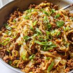 A close-up of a pan filled with a savory Egg Roll in a Bowl, featuring ground meat, cabbage, and green onions.