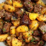 Close-up of tender garlic steak bites mixed with golden roasted potatoes, garnished with fresh parsley.