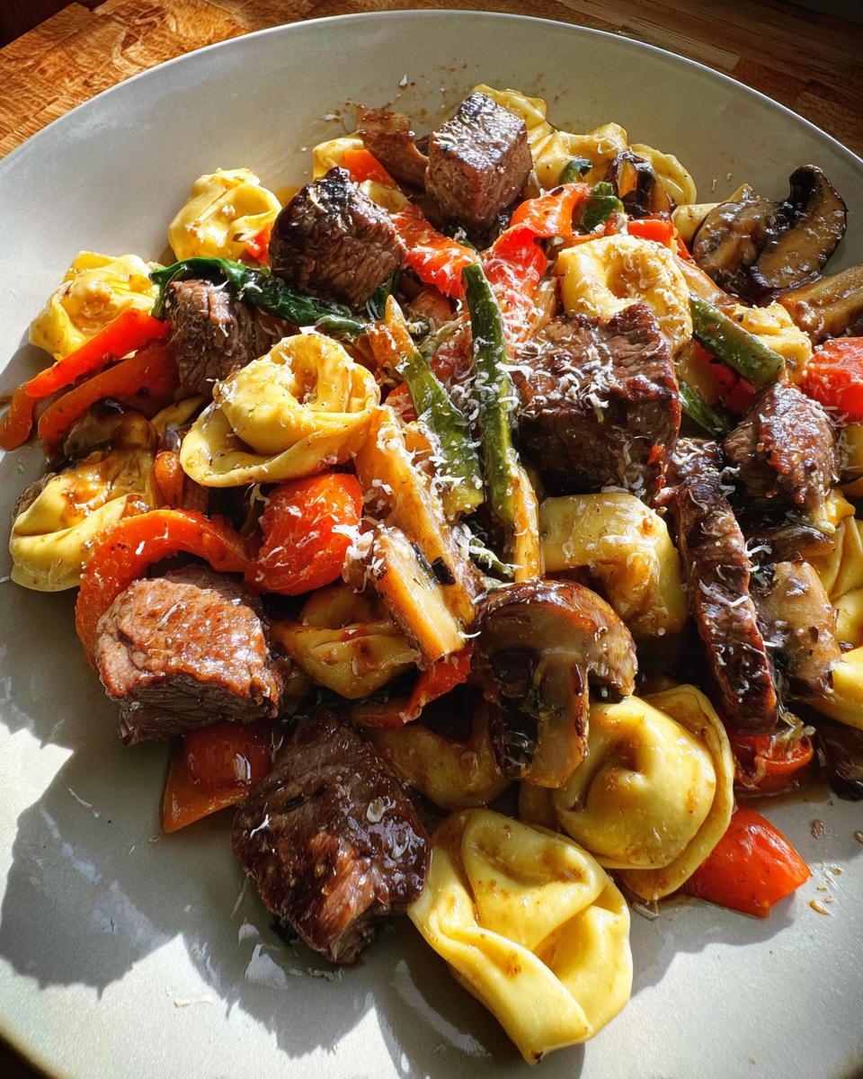 A close-up of a plate filled with Garlic Steak Tortellini, featuring tender steak bites, cheese tortellini, bell peppers, mushrooms, and green beans.
