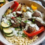 A delicious Greek Meatball Bowl Recipe featuring meatballs, roasted vegetables, couscous, and creamy tzatziki sauce.