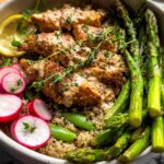 A healthy lemon garlic chicken meal prep bowl with quinoa, asparagus, radishes, and snap peas.