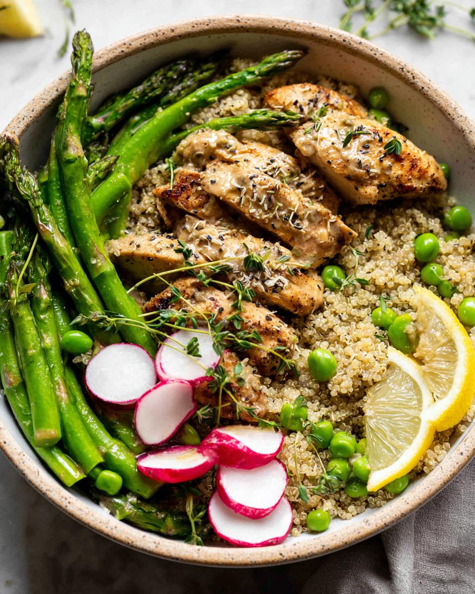 A vibrant Healthy Lemon Garlic Chicken Meal Prep Bowl with quinoa, asparagus, peas, radishes, and lemon.
