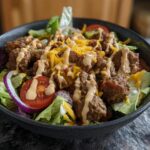 A delicious bowl of High-Protein Cheeseburger Bowls with seasoned ground beef, lettuce, tomatoes, onions, cheese, and dressing.