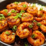 A close-up shot of glistening, pan-seared High-Protein Honey Garlic Shrimp, garnished with chopped green onions.