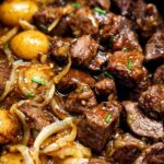 Close-up of tender High Protein Slow Cooker Garlic Butter Beef Bites with onions and baby potatoes in a rich sauce.