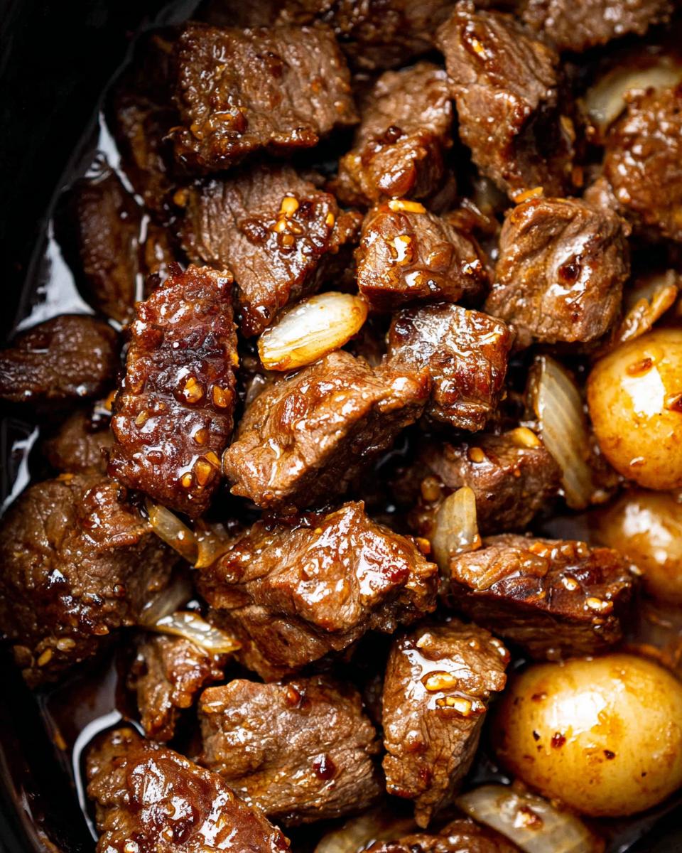 Close-up of tender High Protein Slow Cooker Garlic Butter Beef Bites in a rich sauce with onions.