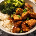 A delicious Honey Garlic Pork Rice Bowl featuring tender pork pieces in a glossy sauce, fluffy white rice, and steamed broccoli florets, garnished with green onions.