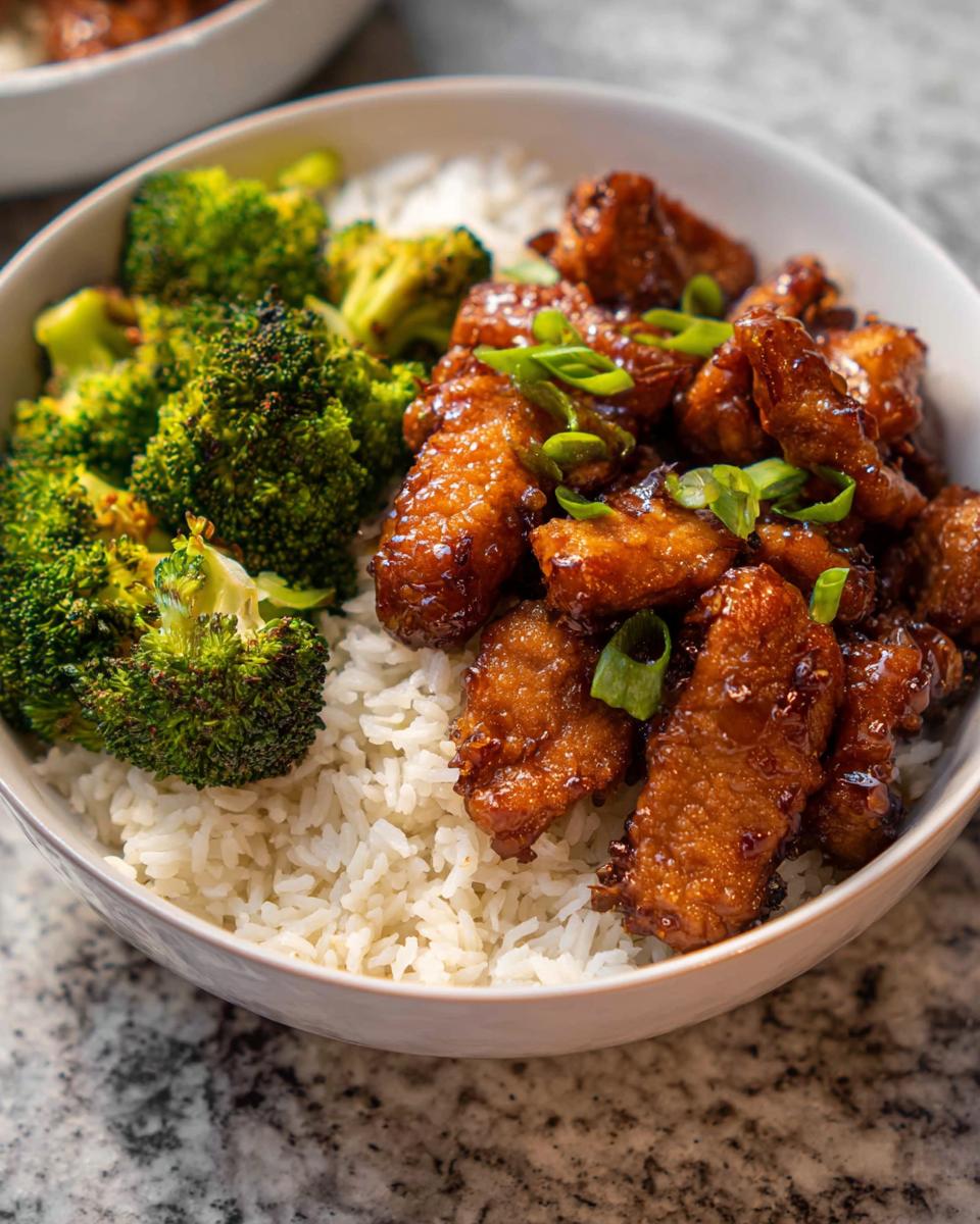 A delicious Honey Garlic Pork Rice Bowl featuring tender pork, fluffy white rice, and steamed broccoli, garnished with green onions.