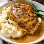 A plate of Irresistible Garlic Herb Chicken served with creamy mashed potatoes and green beans, drizzled with sauce.