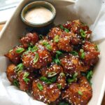 Close-up of Irresistible Sticky Honey Garlic Cauliflower Recipe bites, coated in glaze and sprinkled with sesame seeds and scallions.
