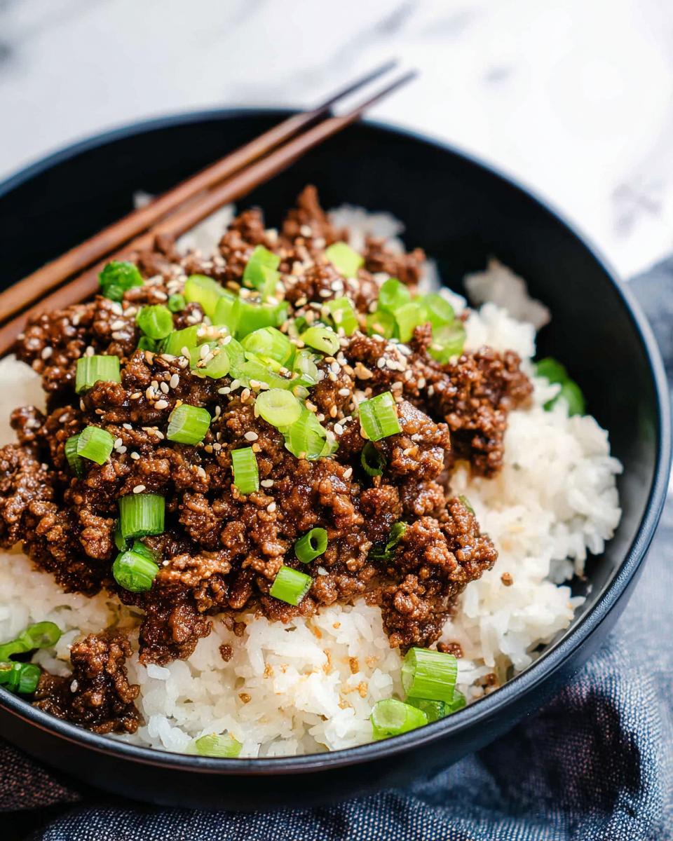 A close-up of a Korean Ground Beef Bowl filled with fluffy white rice and topped with savory ground beef, green onions, and sesame seeds.