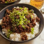 A close-up of a Korean Ground Beef Bowl topped with green onions and sesame seeds, served over white rice.