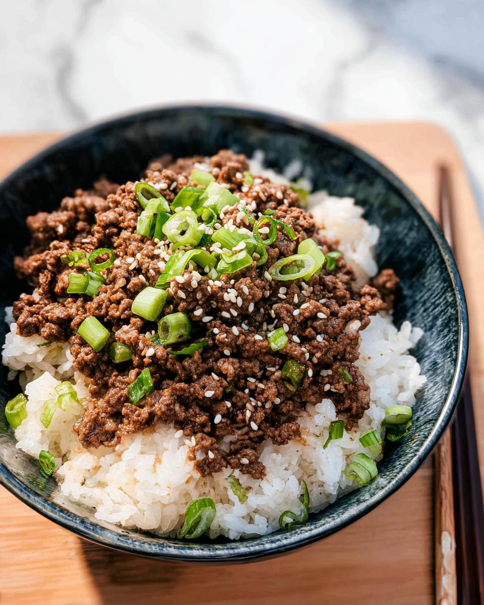 A close-up of a Korean Ground Beef Bowl, featuring seasoned ground beef over fluffy white rice, garnished with green onions and sesame seeds.