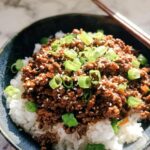 A close-up view of a Korean Ground Beef Bowl, featuring seasoned ground beef over white rice, garnished with green onions and sesame seeds.