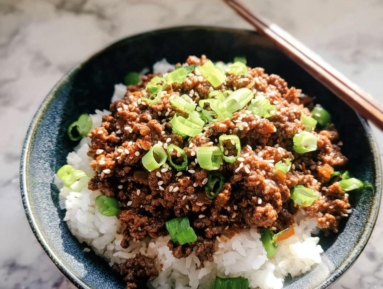 A close-up view of a Korean Ground Beef Bowl, featuring seasoned ground beef over white rice, garnished with green onions and sesame seeds.