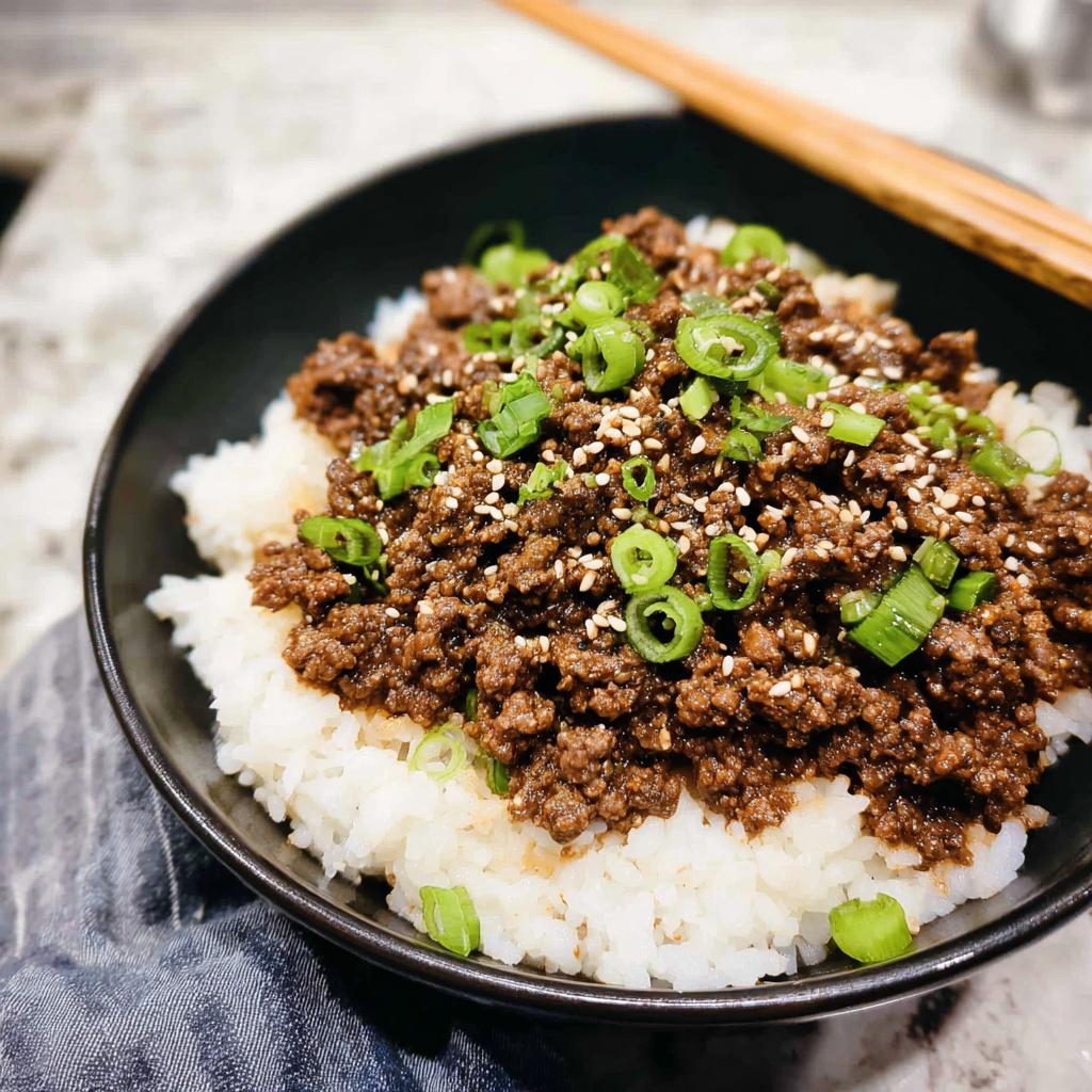 A close-up of a Korean Ground Beef Bowl, topped with chopped green onions and sesame seeds, served over white rice.