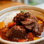 Close-up of a bowl of Korean Style Pot Roast with tender beef, carrots, and white rice, garnished with chili flakes.
