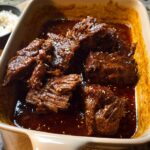 Close-up of tender Korean Style Pot Roast pieces in a rich, dark sauce, sprinkled with sesame seeds.