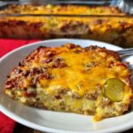 A delicious slice of Low-Carb Bacon Cheeseburger Casserole topped with melted cheddar cheese and a pickle slice.
