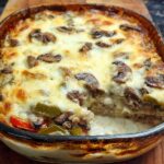 A bubbling Low Carb Philly Cheesesteak Casserole in a baking dish, topped with melted cheese, mushrooms, and peppers.