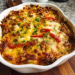 A golden-brown Low Carb Philly Cheesesteak Casserole baked in a white dish, topped with melted cheese and parsley.