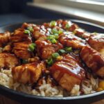 A close-up of a bowl of One-Pan Honey BBQ Chicken Rice, featuring glazed chicken pieces over rice with mixed vegetables.