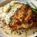 A golden-brown Parmesan Crusted Chicken breast generously topped with creamy garlic sauce and fresh parsley, served with mashed potatoes and green beans.