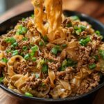 A close-up of a bowl filled with Potsticker Noodle Bowl with Pork & Cabbage Slaw, topped with chopped green onions.
