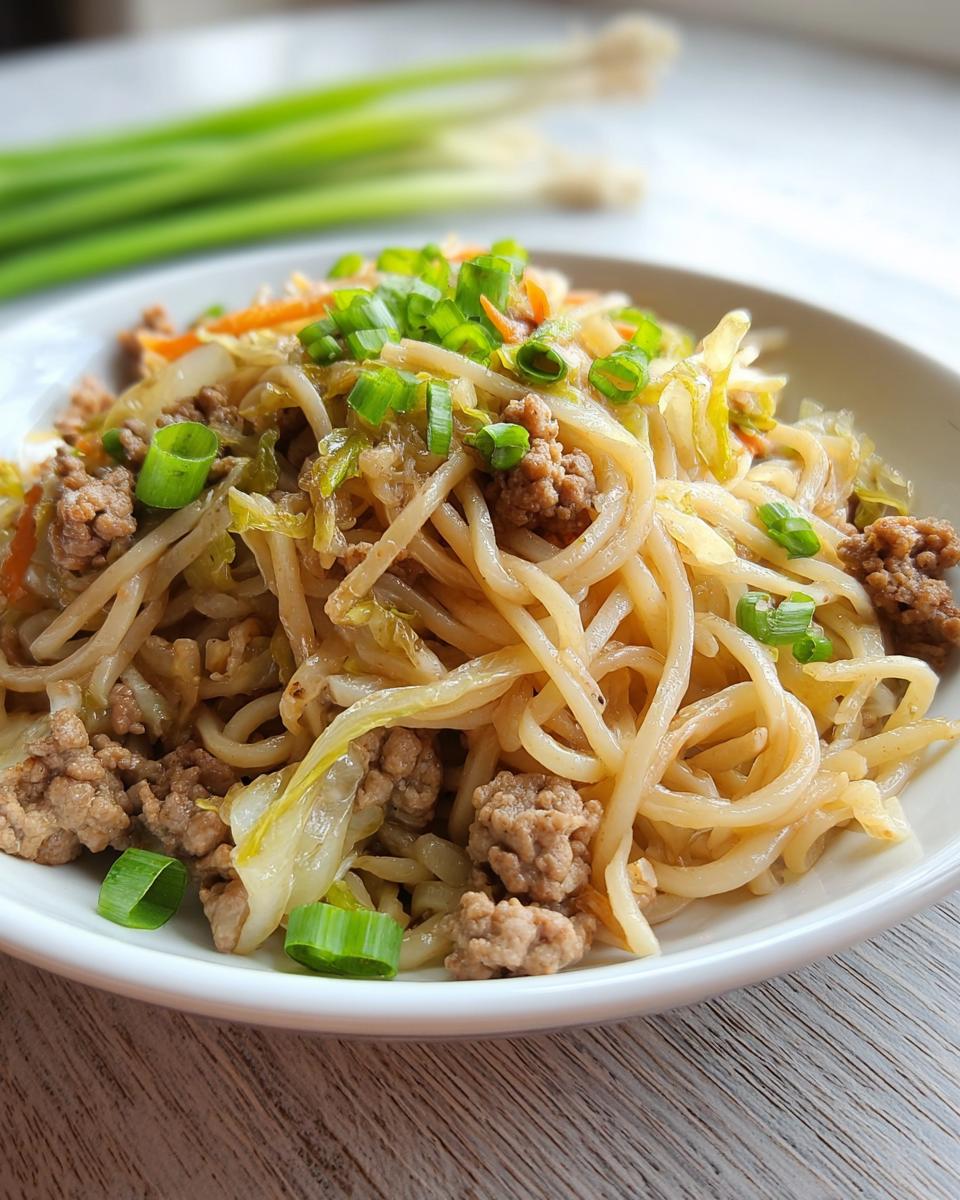 A close-up of a white bowl filled with Potsticker Noodle Bowl with Pork & Cabbage Slaw, garnished with green onions.