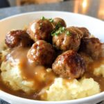 A bowl of Salisbury Steak Meatballs covered in gravy, served over creamy Garlic Herb Mashed Potatoes, garnished with parsley.