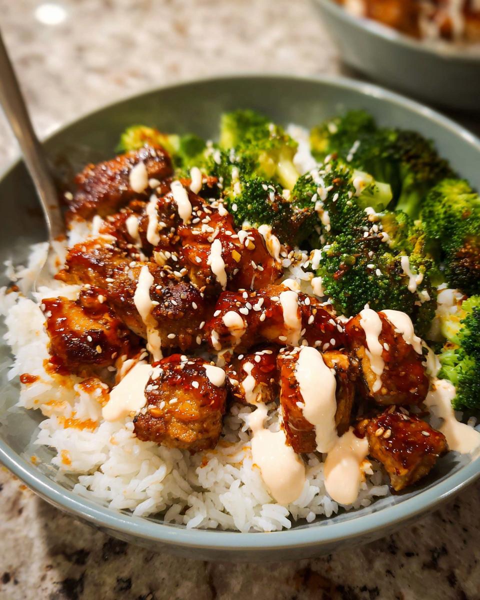 Close-up of a bowl of Sticky Chicken Bowls with rice, broccoli, sesame seeds, and a creamy drizzle.