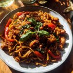A close-up of a plate of Sticky Garlic Chicken Noodles, featuring tender chicken pieces, bell peppers, and fresh basil.