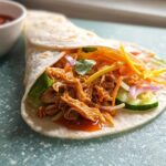 Close-up of a Sweet Chili Chicken Wrap filled with shredded chicken, lettuce, cucumber, carrots, and red onion.
