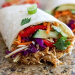A close-up of a Teriyaki Chicken Wrap filled with shredded chicken, colorful vegetables, and topped with scallions.