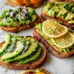 Close-up of various avocado toast toppings including sliced avocado, lemon, and red onion.