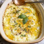 A close-up of baked feta eggs in a rustic ceramic dish, topped with fresh basil and drizzled with olive oil.