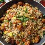 A bowl of flavorful Bang Bang Fried Rice with tender chicken pieces, scrambled eggs, peas, and carrots, garnished with green onions.