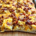Close-up of a slice of breakfast pizza egg recipe, topped with scrambled eggs, cheese, and crispy bacon.