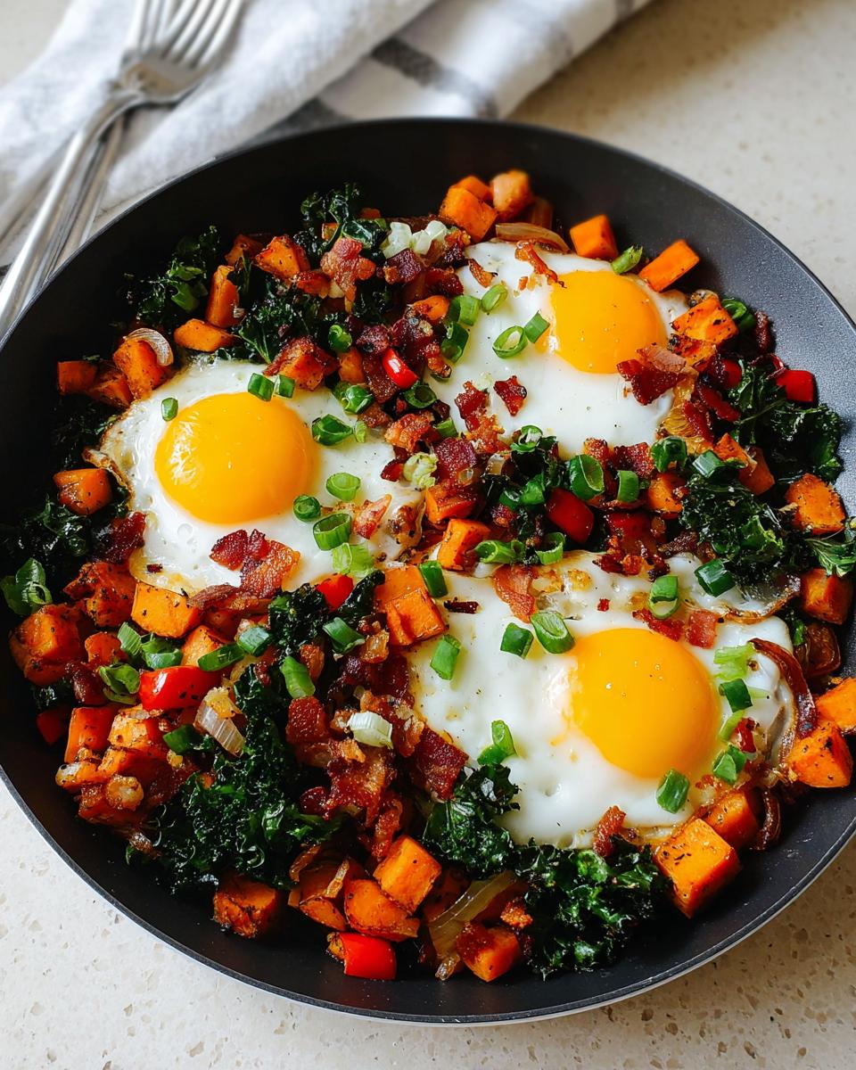 A hearty BREAKFAST SWEET POTATO hash with fried eggs, crispy bacon, kale, and green onions in a black skillet.