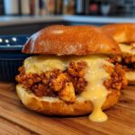 Two delicious Cajun Chicken Sloppy Joes topped with creamy cheese sauce on a wooden board.