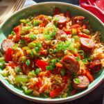 A close-up overhead view of a Cajun Sausage and Rice Skillet, featuring sliced sausage, rice, bell peppers, and green onions.