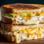 A stack of two delicious Chicken Avocado Melt Sandwiches with melted cheese and sliced avocado.