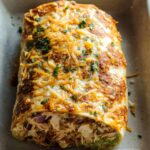 A close-up of a golden-brown Chicken Avocado Ranch Burrito topped with melted cheese and parsley.