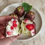 A hand holding a chocolate-covered strawberry yogurt cluster, revealing freeze-dried strawberries and creamy yogurt inside. Chocolate Strawberry Yogurt Clusters Recipe.