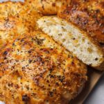 Close-up of freshly baked cottage cheese flagels, one sliced open to reveal a fluffy interior, topped with everything bagel seasoning.