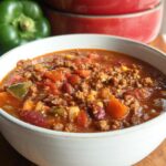 A close-up of a steaming bowl of Cowboy Soup, filled with ground beef, beans, corn, and tomatoes.