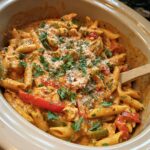 A close-up view of Crock Pot Creamy Cajun Chicken Pasta in a slow cooker, garnished with parsley and cheese.