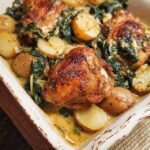 A close-up of a creamy dish featuring golden-brown Garlic Parmesan Chicken Thighs and tender baby potatoes with spinach.