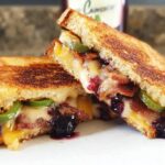 A gourmet blueberry grilled cheese sandwich cut in half, revealing melted cheese, blueberries, bacon, and jalapenos.